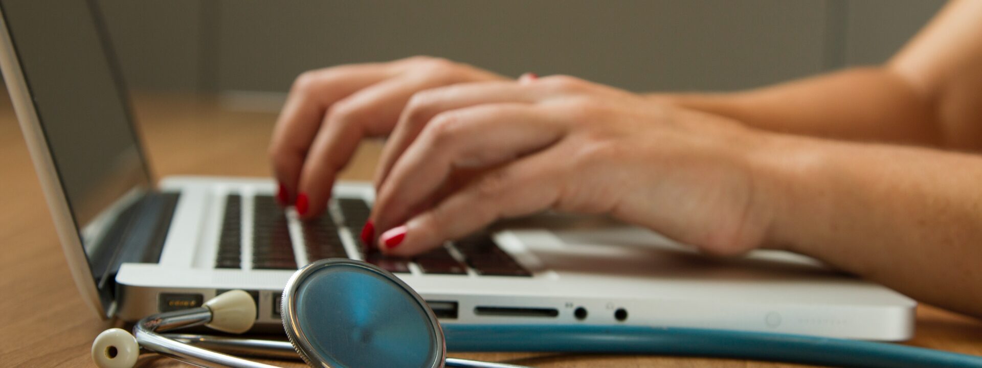 medecin tapant au clavier d'un macbook devant un stétoscope bleu